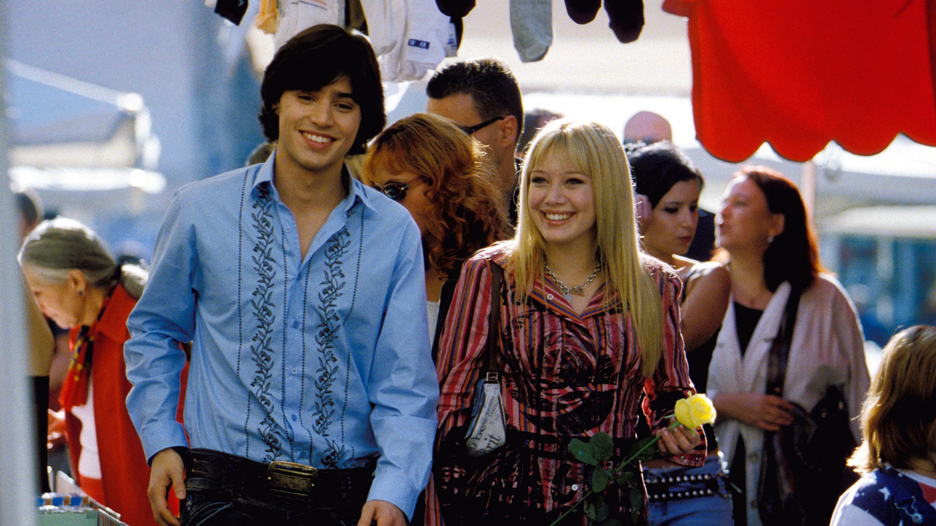 Paolo and Lizzie walking happily through a Rome market, Lizzie holding a yellow rose